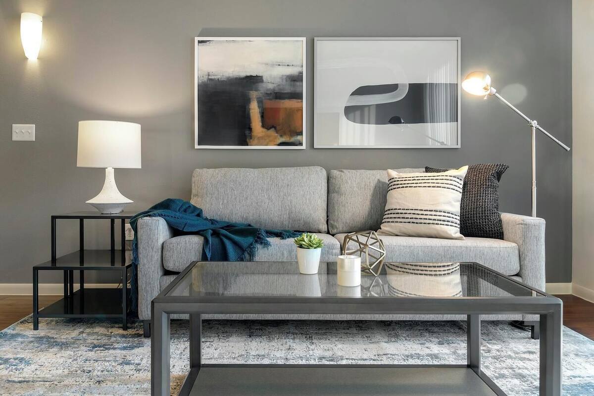 A modern living room with a grey sofa, a glass coffee table, a lamp, and abstract wall art.