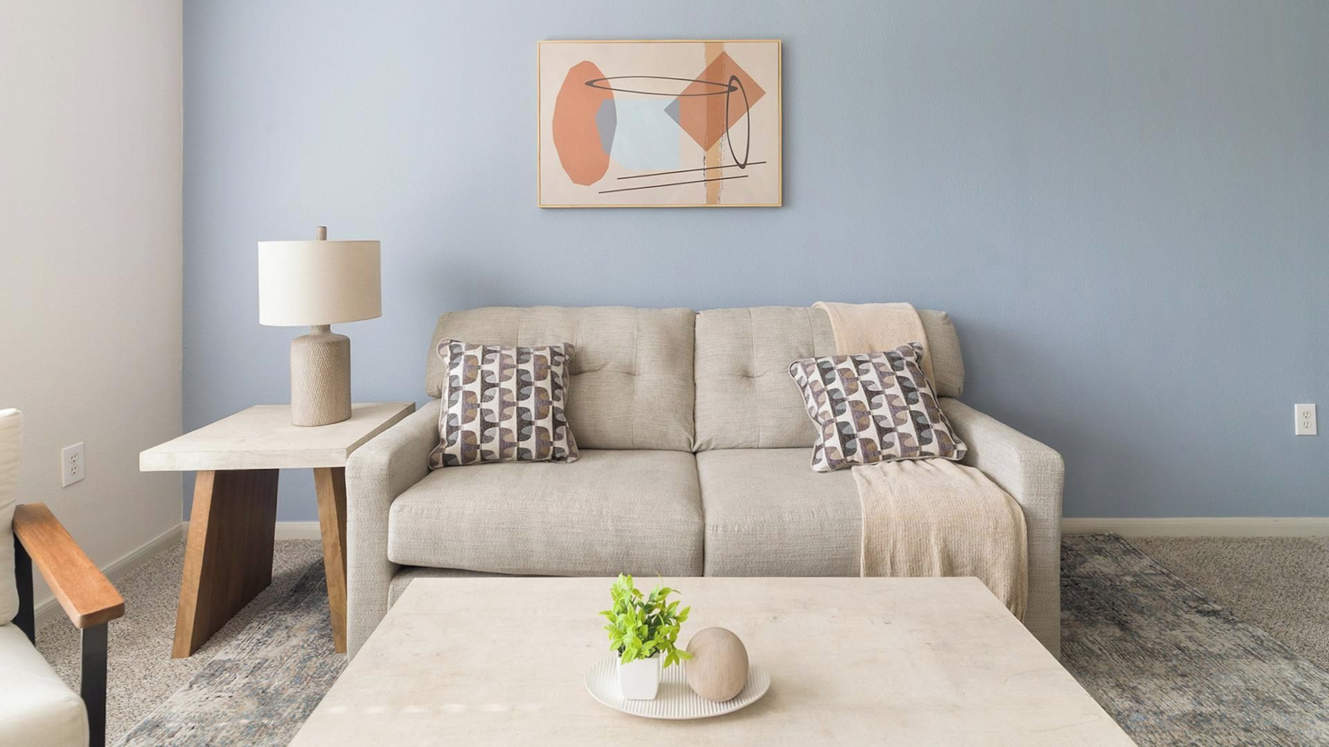 A living room with a sofa, a coffee table, a lamp, and a wall art piece.