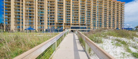 A long, narrow wooden boardwalk leading to a large, multi-story hotel with balconies.