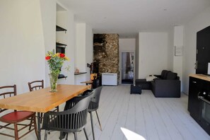 A modern living space with a dining area, a stone accent wall, a sofa, and a kitchen. - Charming ground floor rental in the center of Luchon (Bagnères-de-Luchon)