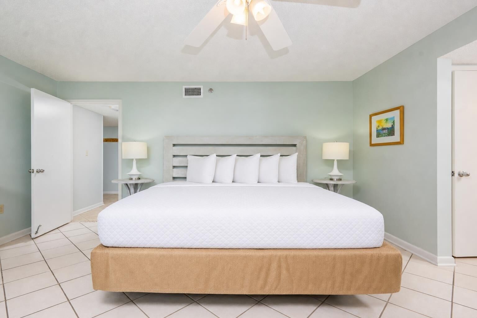 Une chambre à coucher avec un lit, deux tables de chevet, un ventilateur de plafond et une porte.