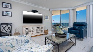 Uma sala de estar com televisão de tela plana, uma poltrona de couro azul, um sofá estampado e um armário branco.