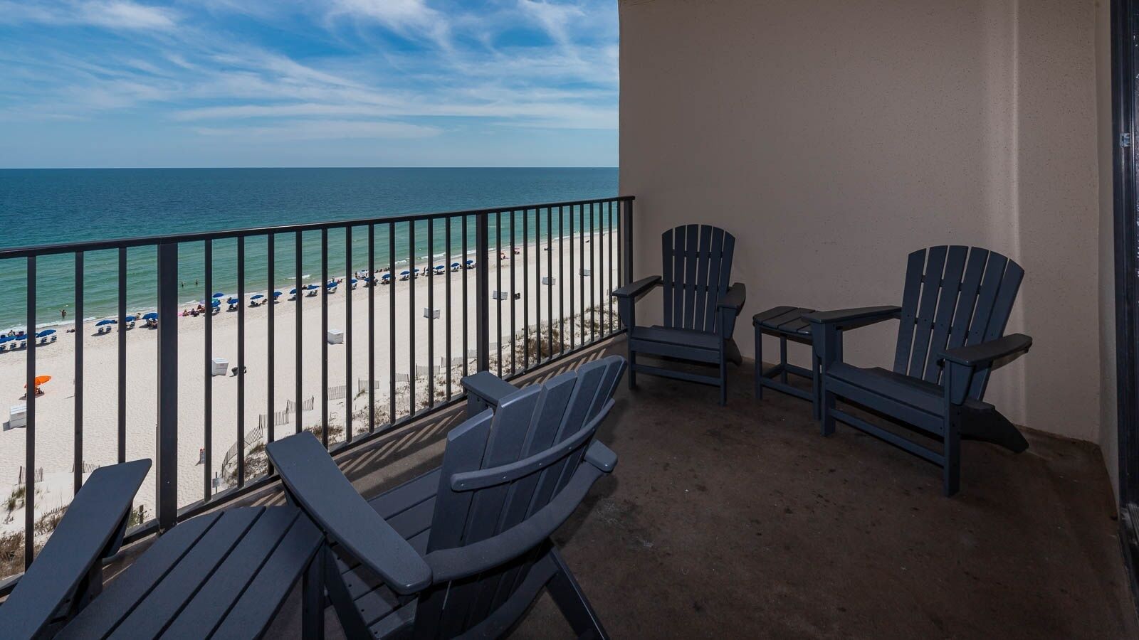Ein Balkon mit zwei Adirondack-Stühlen, einem kleinen Tisch und Blick auf den Strand und das Meer.