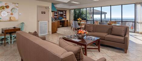A spacious living area with a large window offering a view of the sea, a comfortable sofa, a coffee table with magazines, and a bookshelf.