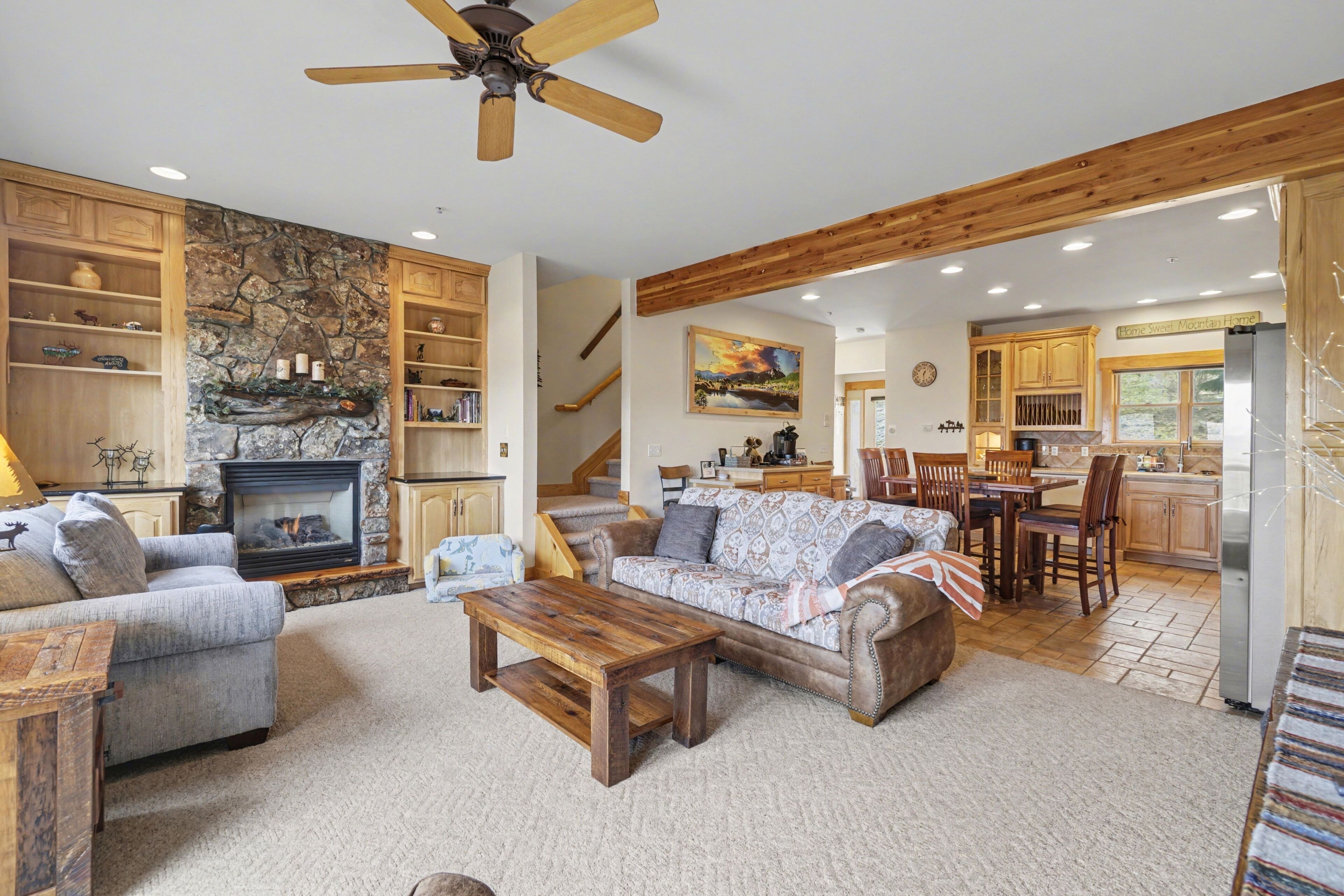A spacious living area with a fireplace, wooden furniture, and a kitchen in the background.