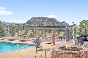 Zona de piscina con sillones de descanso, una chimenea y vistas a la montaña.