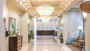A hotel lobby with a chandelier, reception desk, seating area, and a sign reading 'The Coffee'. - Gulfview Retreat At The Palms 2 Bedroom Condo (Destin)