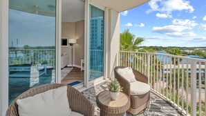 A balcony with wicker furniture, a potted plant, and a view of a pool and palm trees. - Gulfview Retreat At The Palms 2 Bedroom Condo (Destin)