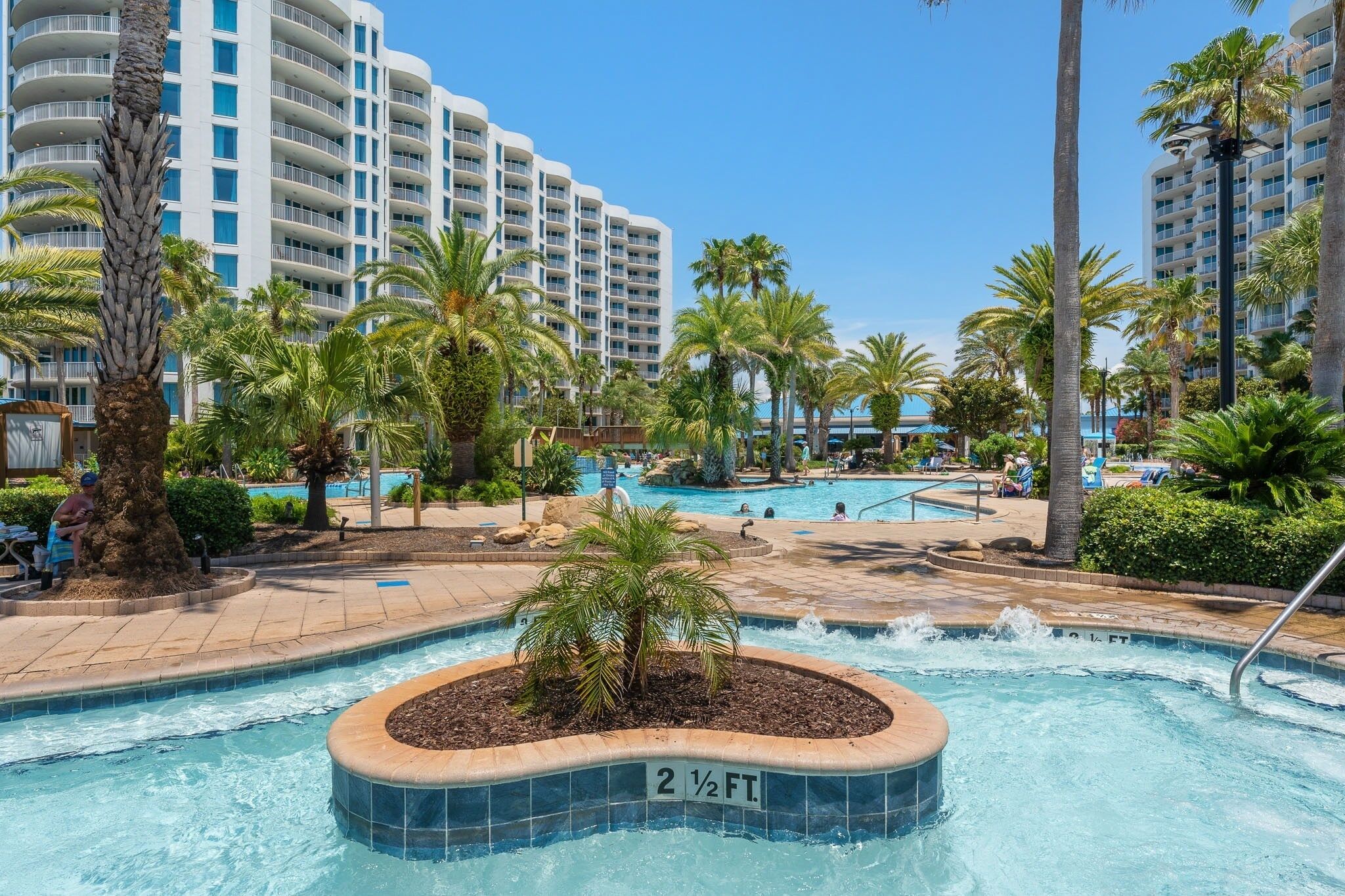 A hotel pool area with palm trees, a hot tub, and a sign indicating the pool's depth.