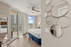 A hotel room with a bed, a ceiling fan, a balcony with a view of buildings, and decorative mirrors on the wall. - Gulfview Retreat At The Palms 2 Bedroom Condo (Destin)