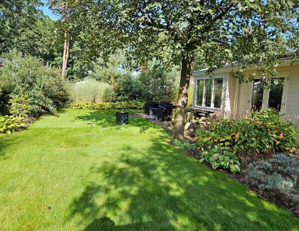 A well-maintained garden with a lawn, a wooden deck, and a house with a covered porch.