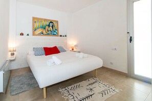 Quarto com cama, duas mesas de cabeceira, um quadro na parede, uma porta e um tapete.