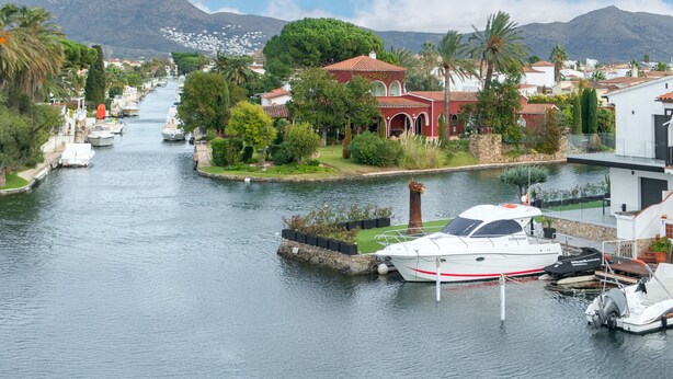 A canal with boats, a red building with arches, and mountains in the background. - WELCS STUDIO 301 EMP with view of the canal (Empuriabrava)