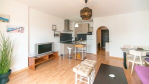 A modern living room with a TV, seating, a dining area, and a kitchen in the background. - WELCS STUDIO 301 EMP with view of the canal (Empuriabrava)