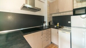 A compact kitchen with a black countertop, wooden cabinets, a stainless steel range hood, a microwave, and a built-in oven. - WELCS STUDIO 301 EMP with view of the canal (Empuriabrava)