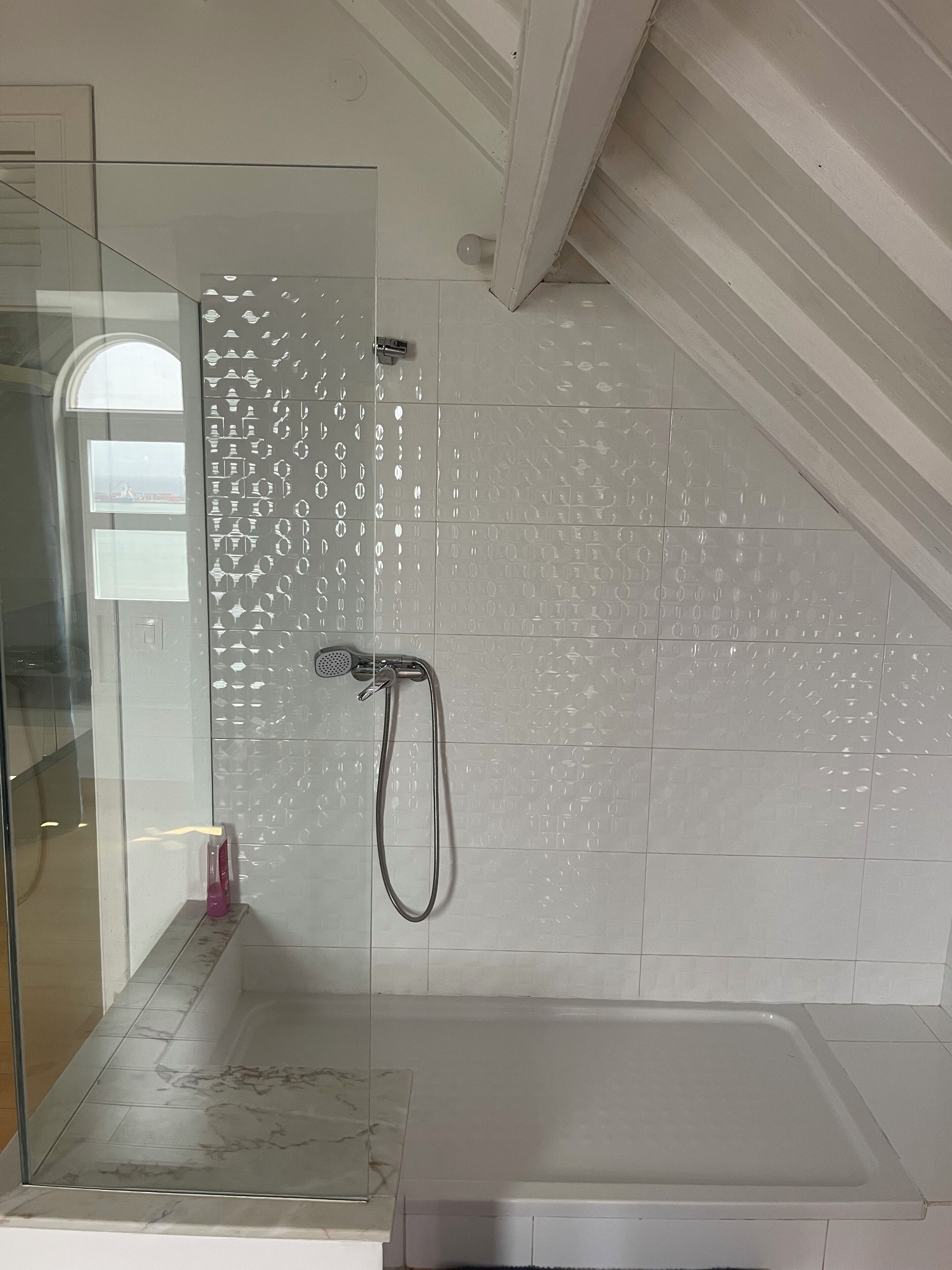 Un baño con cabina de ducha de vidrio, bañera y pared revestida de azulejos con motivo de diamante.