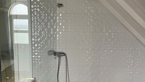 Ein Badezimmer mit Duschabtrennung aus Glas, einer Badewanne und einer mit Rautenmuster gefliesten Wand.
