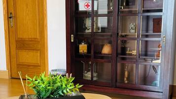 Una puerta de madera, una mesa redonda con un cartel de bienvenida, un aparador de madera oscura con puertas de cristal y tres relojes de pared.