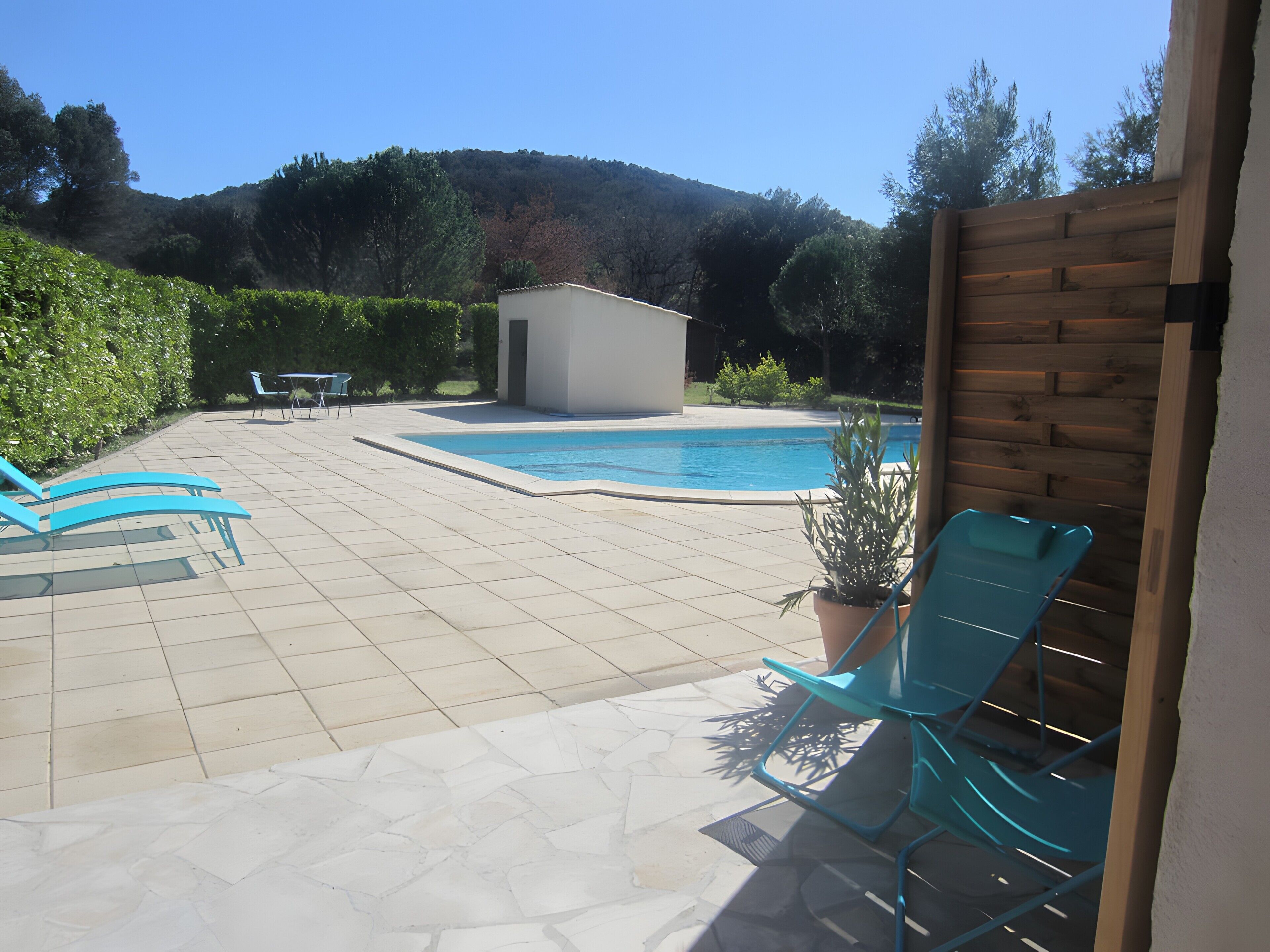 A swimming pool with a tiled deck, a small shed, and a wooden fence.
