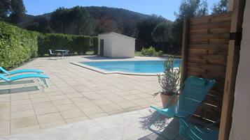 A swimming pool with a tiled deck, a small shed, and a wooden fence.