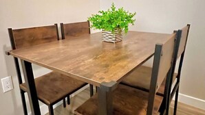 Une table à manger avec des chaises, une plante en pot et deux œuvres d’art encadrées accrochées au mur.