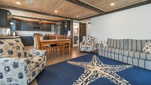 Ein modernes Interieur mit Holzboden, einem Essbereich mit Holztisch und -stühlen, einem gestreiften Sofa und einem Teppich mit Sternenmuster.
