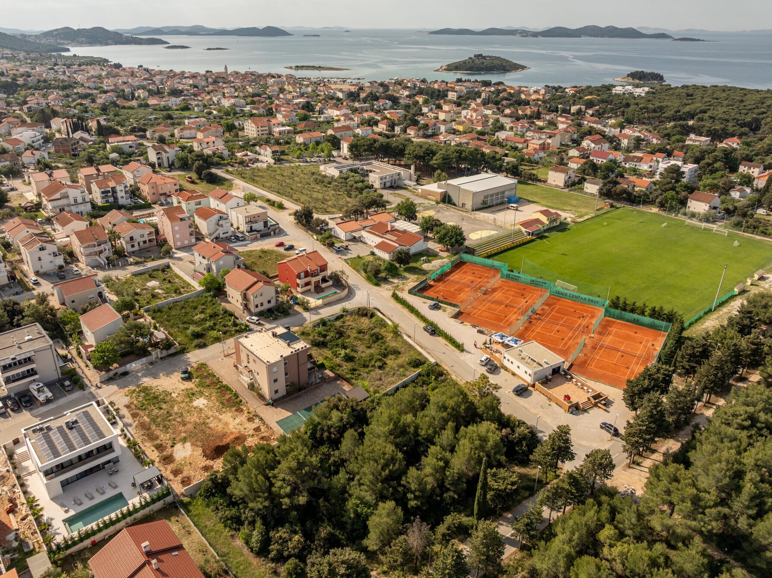 Vista aérea de una zona residencial con casas, una cancha de tenis y una piscina.