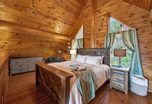 Dormitorio de cabaña de madera con cama, mesita de noche, lámpara y ventana con cortinas.