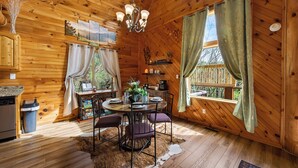 Ein Holzblock-Interieur mit einem Esstisch, Stühlen, einer Kronleuchter und Blick ins Freie.
