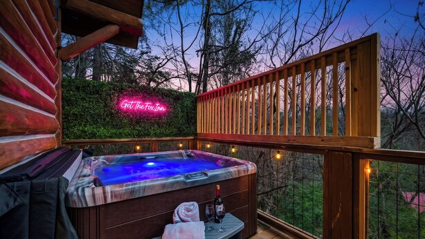 Ein Whirlpool mit Sitzbank und Handtuch, eine Neonreklame und eine Holzterrasse mit Blick auf Bäume.
