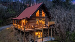 Eine Holzhütte mit rotem Dach, einer Terrasse mit Lichterketten und einem Steinfundament.