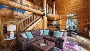 Ein Holzinnenraum mit einem braunen Ecksofa, einem kleinen Tisch mit Flasche und Gläsern, einer Treppe und einem Essbereich mit Tisch und Stühlen.