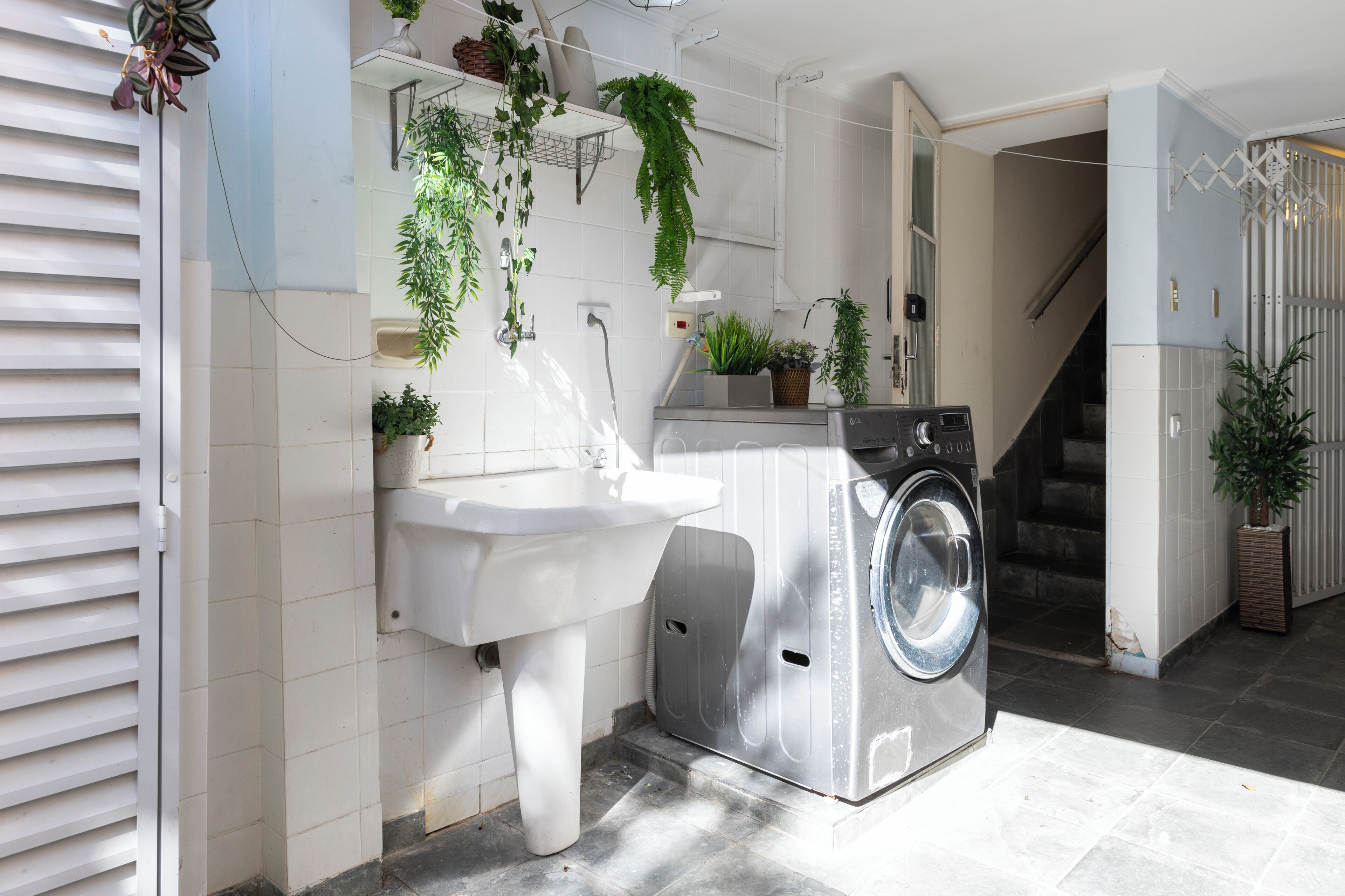 A compact laundry area with a washing machine, a sink, and various potted plants.