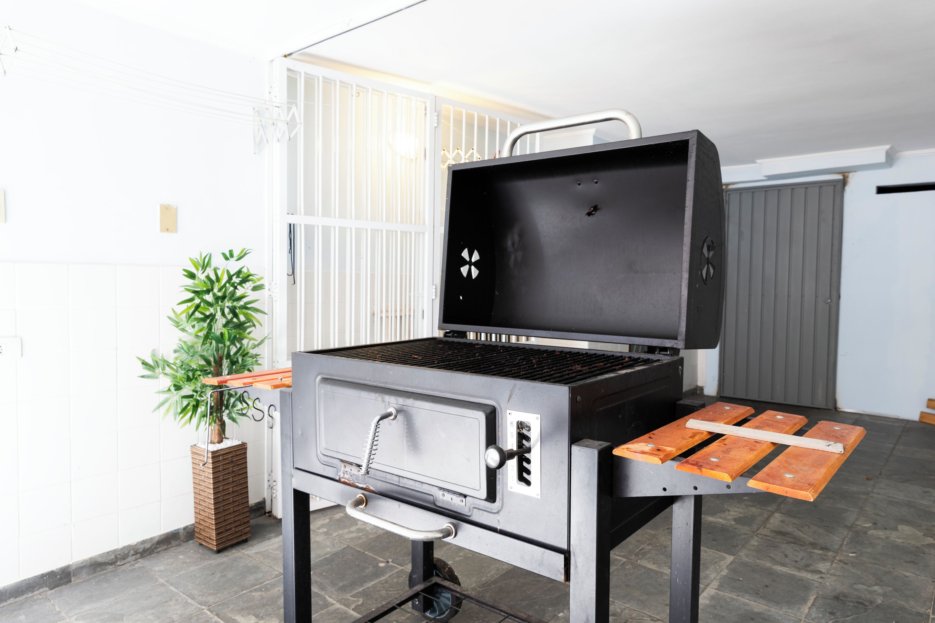 A portable grill with a control panel and a side table, placed on a tiled floor.