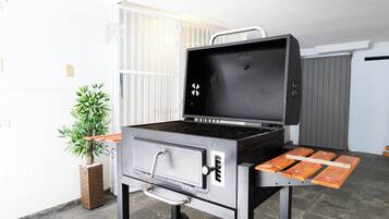 A portable grill with a control panel and a side table, placed on a tiled floor.