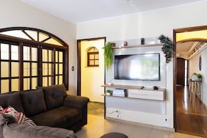 A living room with a sofa, a TV mounted on the wall, and a wooden door with glass panels. - Casa de 4 quartos com AC no Ipiranga (São Paulo)