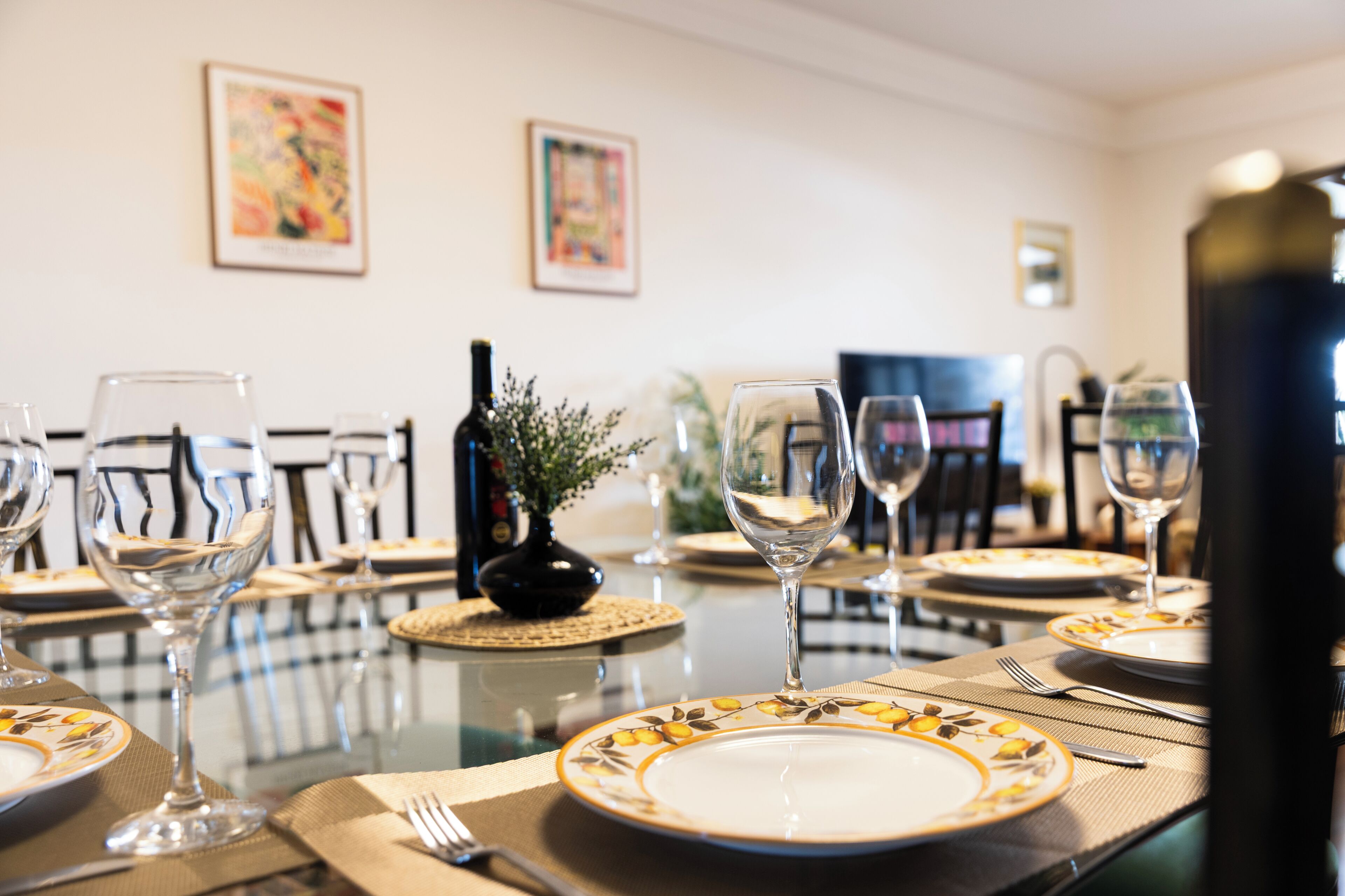A dining table set with plates, glasses, and cutlery, with a bottle and a small plant on the table.
