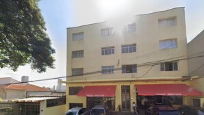 A multi-story building with a yellow facade and red awnings. There are several windows, some with shutters, and a visible entrance with a sign. - Casa de 4 quartos com AC no Ipiranga (São Paulo)