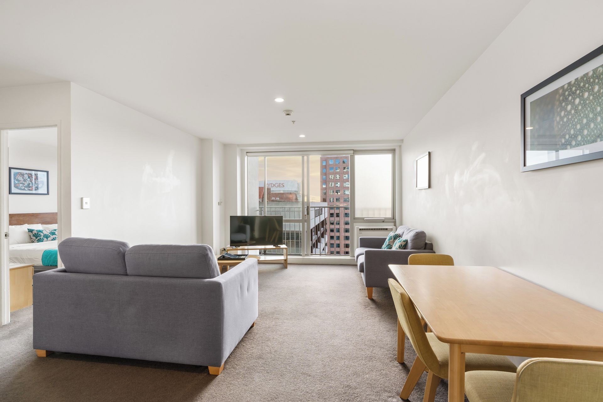 A modern living room with a grey sofa, a wooden dining table, and a TV.