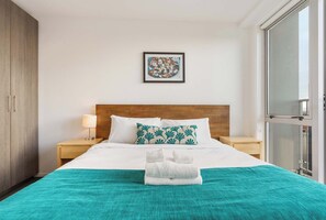 Una habitación de hotel con una cama, una mesita de noche, una lámpara, un cuadro en la pared y una ventana.