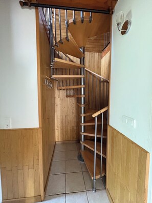 A wooden staircase with metal railings, a tiled floor, and a light switch on the wall.