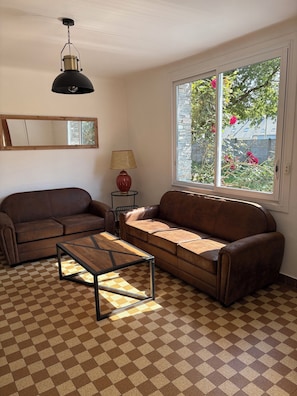 A living room with two brown leather sofas, a wooden coffee table, a lamp, a mirror, and a window with a view of greenery. - House 250m from Pont-Mahé beach "the Mediterranean of the west". (Assérac)