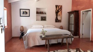 Quarto com cama, um banco de madeira, um tapete de couro de vaca, guarda-roupa e obras de arte nas paredes.