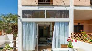 Ein zweistöckiges Gebäude mit Balkon, einer mit Vorhängen versehenen Tür, einem kleinen Tisch mit Pflanze und einem Holzzaun.
