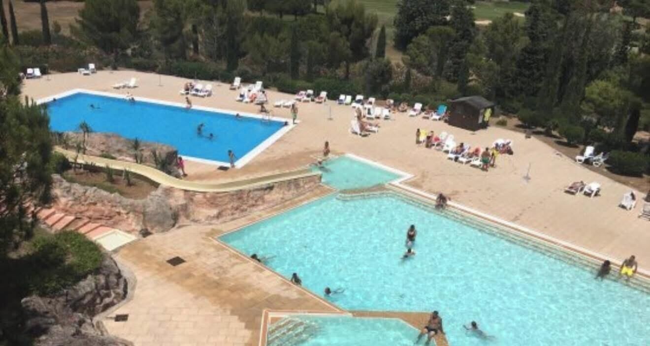 A large outdoor swimming pool with multiple lanes, surrounded by lounge chairs and sunbeds.