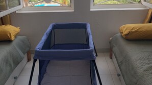 Ein Zimmer mit Blick auf einen Pool und viel Grün, ein blaues Treppenschutzgitter, zwei grüne Betten mit gelben Kissen und eine Tafel mit Text.