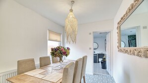 En matplats med ett träbord, beige stolar, en kristallkrona och en vas med blommor.