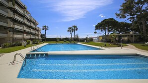 Une piscine, un ciel bleu dégagé, des palmiers et, au loin, un immeuble à plusieurs étages.