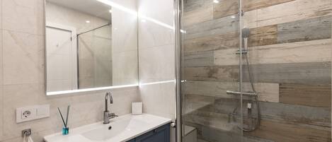 Une salle de bain moderne avec une douche à l’italienne en verre, un lavabo blanc et un grand miroir.