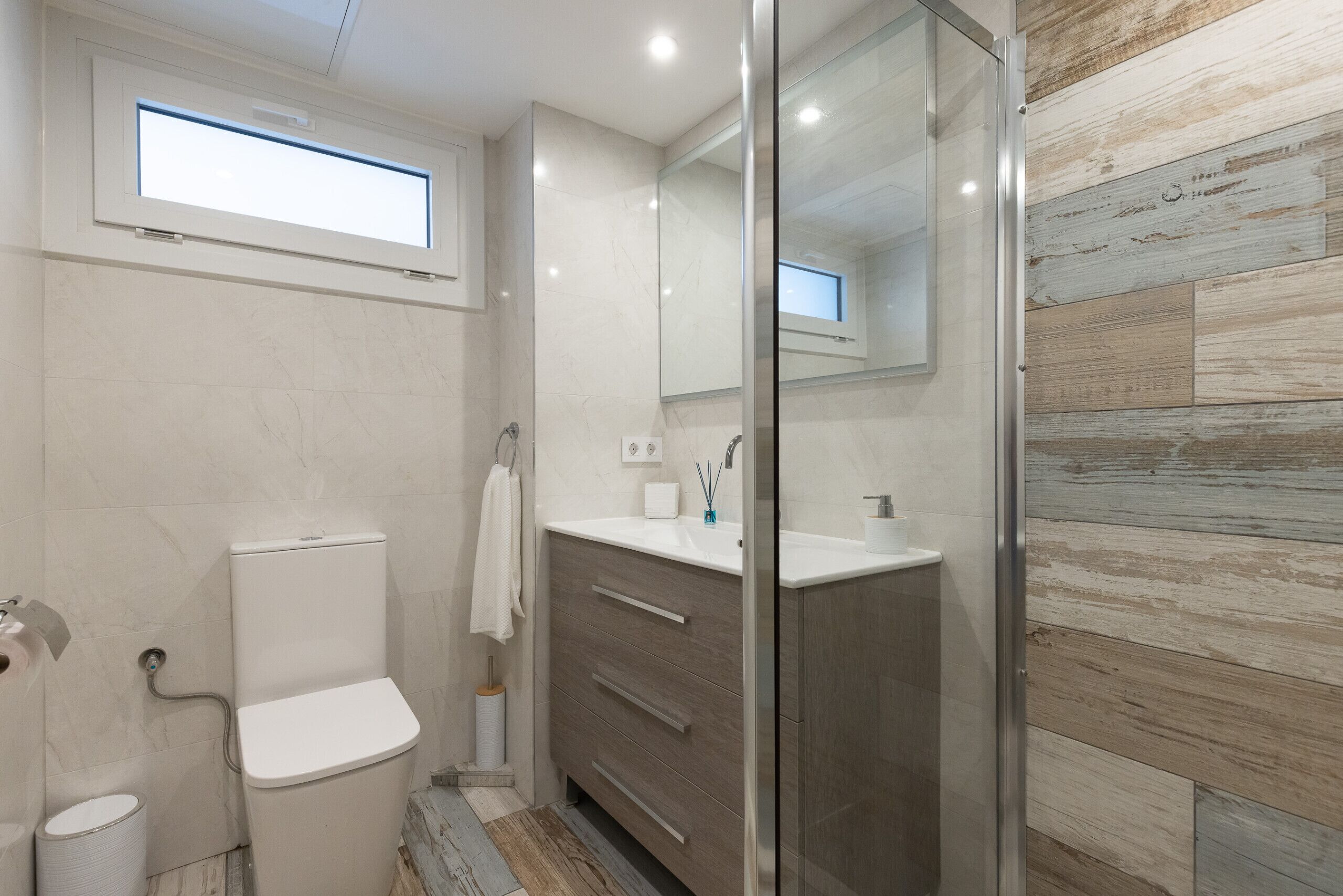 A modern bathroom with a toilet, sink, vanity, and a glass shower enclosure.